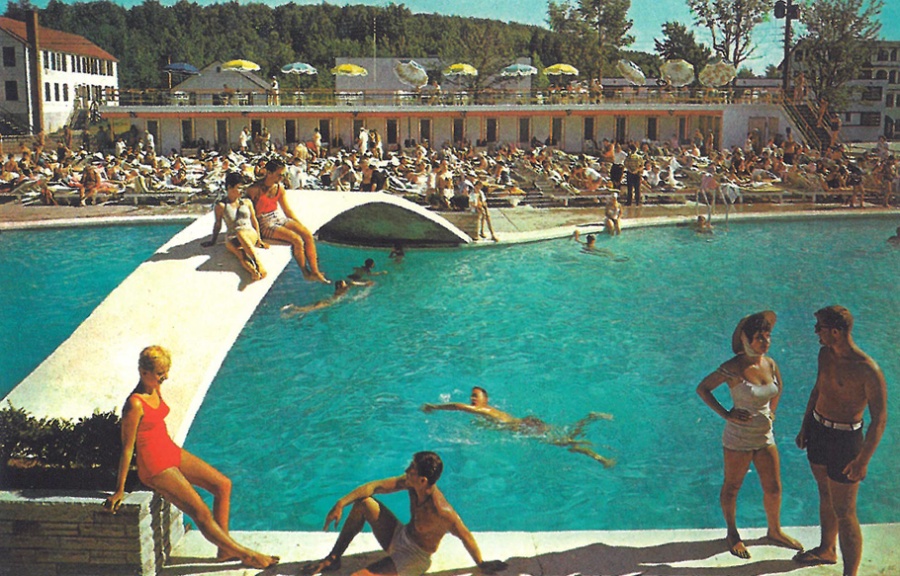 Historic postcard of outdoor pool with bridge over center and lots of people sunbathing on opposite side of pool