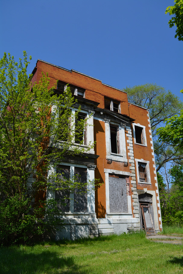 Exterior of tan brick abandoned apartment house in residential area of Detroit